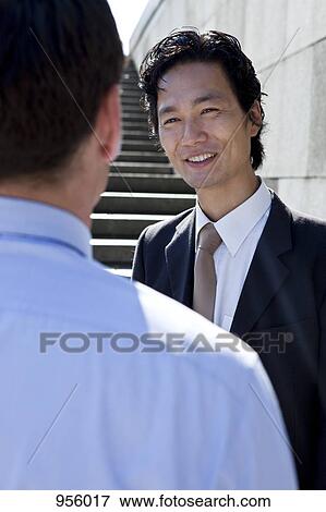 A businessman talking to a colleague, outdoors, over the shoulder view View Large Photo Image Stock Photo - A businessman talking to a colleague, outdoors, over the shoulder view. Fotosearch