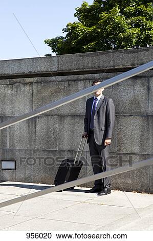 A businessman with a wheeled suitcase, face obscured by railing View Large Photo Image Stock Image - A businessman with a wheeled suitcase, face obscured by railing. Fotosearch