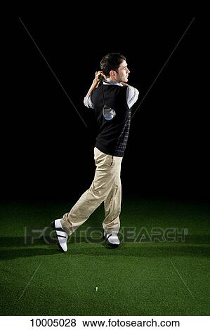 Stock Photo - A golfer swinging a club, portrait, studio shot. Fotosearch