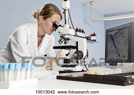Stock Image - A lab technician looking into a microscope in a laboratory. Fotosearch