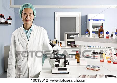 A lab technician standing next to a microscope, looking at camera View Large Photo Image Stock Image - A lab technician standing next to a microscope, looking at camera. Fotosearch