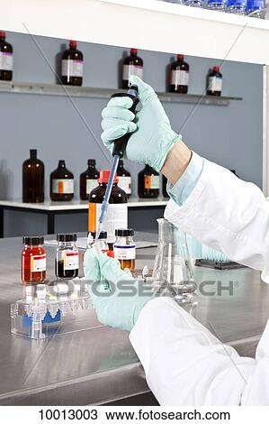 Stock Image - A lab technician using a dropper to put liquid into test tubes, close-up of hands . Fotosearch