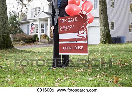 Stock Photography - A real estate agent standing by a FOR SALE sign. Fotosearch