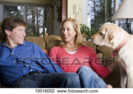 Stock Image - A smiling couple sitting on a couch with their dog. Fotosearch