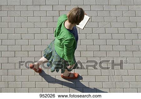Stock Photograph - A woman walking and reading a book. Fotosearch