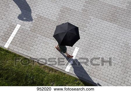 Stock Image - A woman walking through a plaza holding an umbrella. Fotosearch