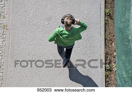 A woman wearing headphones walking on a sidewalk View Large Photo Image Stock Image - A woman wearing headphones walking on a sidewalk. Fotosearch