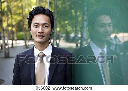 Stock Image - Portrait of a businessman leaning against a window, outdoors. Fotosearch