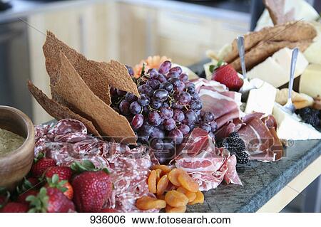 Stock Photograph - Selection of cold meats, cheeses and fruits on a kitchen counter. Fotosearch