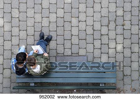 Two boys sitting on a park bench looking at a book View Large Photo Image Stock Image - Two boys sitting on a park bench looking at a book. Fotosearch