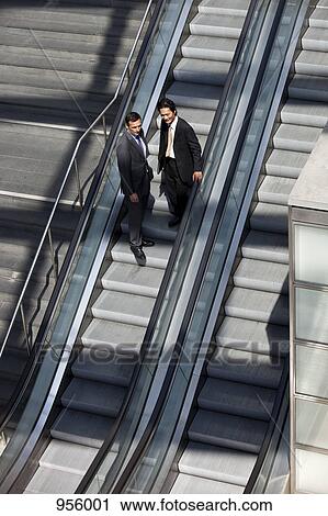 Two businessmen riding down an escalator View Large Photo Image Stock Image - Two businessmen riding down an escalator. Fotosearch