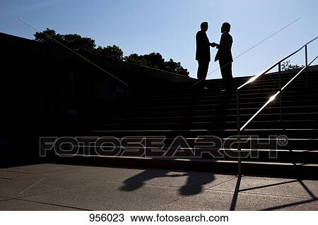 Stock Image - Two businessmen shaking hands, outdoors, silhouette. Fotosearch