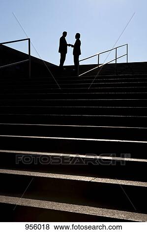 Stock Photo - Two businessmen shaking hands, outdoors, silhouette. Fotosearch