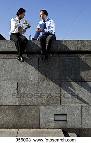 Two businessmen sitting on a wall during a lunch break View Large Photo Image Stock Image - Two businessmen sitting on a wall during a lunch break. Fotosearch