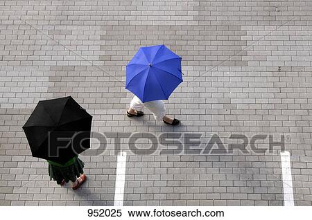 Two women with umbrellas walking through a parking lot View Large Photo Image Stock Photography - Two women with umbrellas walking through a parking lot. Fotosearch