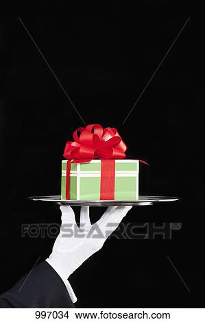 A butler presenting a gift on a silver tray, focus on hand View Large Photo Image Picture - A butler presenting a gift on a silver tray, focus on hand. Fotosearch