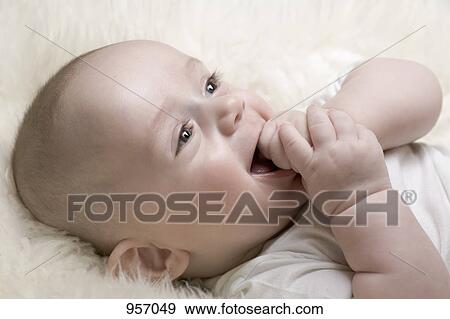 Stock Photo - A cheerful baby with his hand in his mouth. Fotosearch