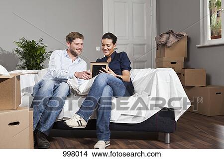 Picture - A couple sitting on a sofa looking at a picture frame. Fotosearch