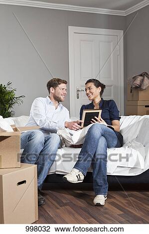 A couple sitting on a sofa looking at a picture frame View Large Photo Image Stock Image - A couple sitting on a sofa looking at a picture frame. Fotosearch