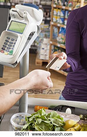 Stock Image - A customer handing a cashier a credit card at the supermarket. Fotosearch