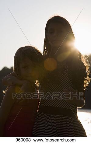 Stock Photo - A girl with her arm around her little sister, portrait. Fotosearch