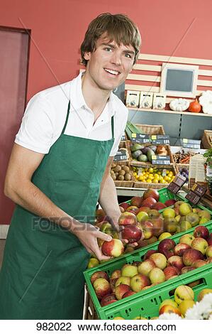 Stock Image - A grocery stocker stocking apples. Fotosearch