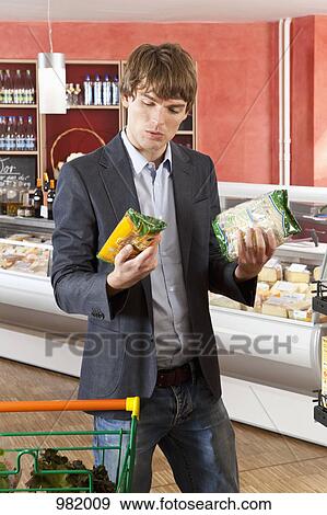 Stock Photo - A man contemplation two products in a supermarket. Fotosearch