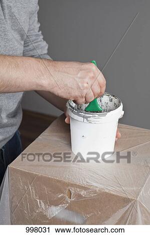 Stock Image - A man dipping a paintbrush into a paint can, focus on midsection, hand. Fotosearch