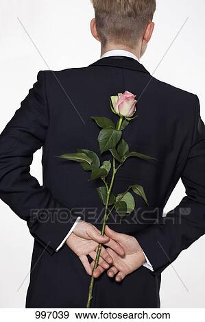 Stock Photo - A man holding a rose behind his back, rear view, waist up. Fotosearch
