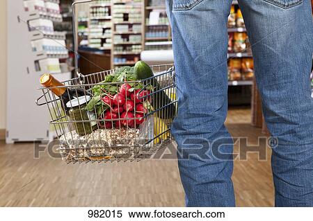 Stock Photography - A man in a supermarket with a full shopping basket, low section. Fotosearch