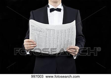 Stock Image - A man in a tuxedo holding a finance newspaper, midsection. Fotosearch