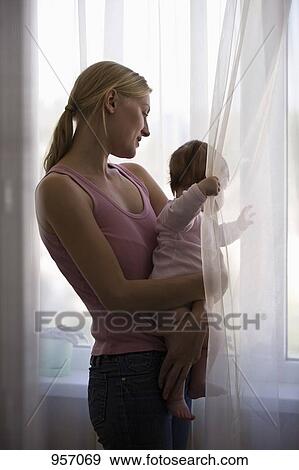Stock Photo - A mother and her baby daughter looking out a window. Fotosearch