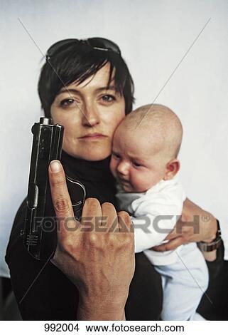 Picture - A mother holding a handgun up and a baby in her other arm. Fotosearch