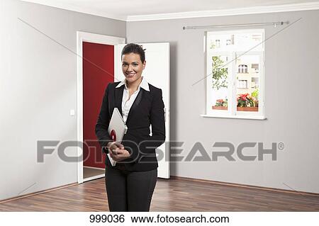 A real estate standing in an empty room holding a laptop View Large Photo Image Stock Photograph - A real estate standing in an empty room holding a laptop. Fotosearch