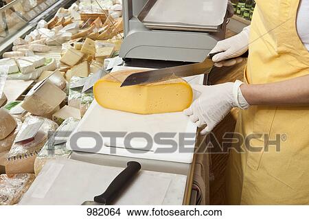 A sales clerk slicing cheese at the cheese counter View Large Photo Image Picture - A sales clerk slicing cheese at the cheese counter. Fotosearch