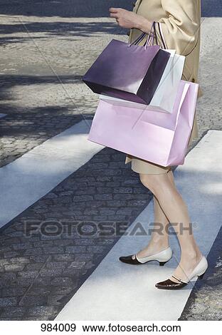 Stock Photo - A woman carrying shopping bags walking across a zebra crossing. Fotosearch