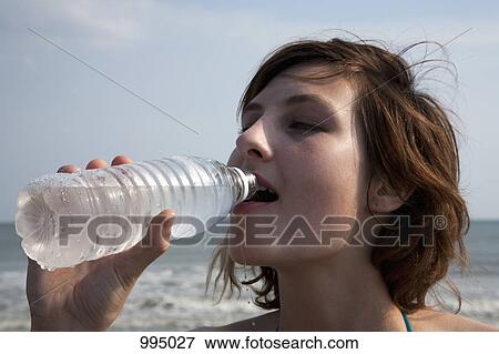 A woman drinking bottled water at the beach View Large Photo Image Stock Photo - A woman drinking bottled water at the beach. Fotosearch