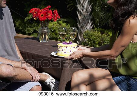 Stock Photograph - A woman giving her boyfriend a birthday cake on a backyard deck. Fotosearch