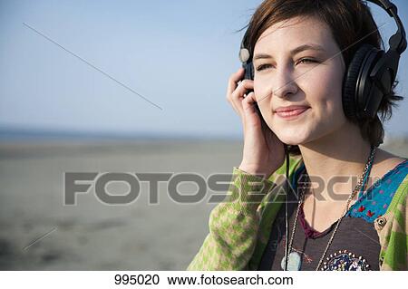 Stock Image - A woman listening to headphones at the beach. Fotosearch