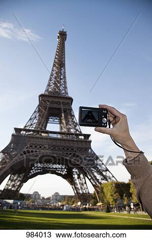Stock Image - A woman photographing the Eiffel Tower, focus on hand. Fotosearch