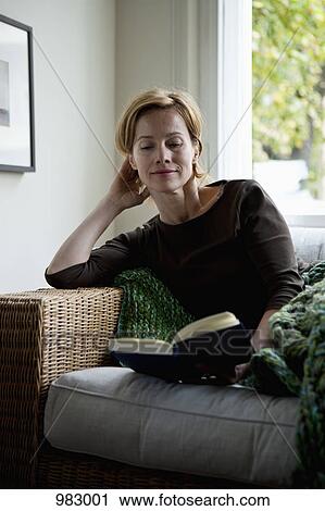 A woman reading a book while reclining on a sofa View Large Photo Image Stock Image - A woman reading a book while reclining on a sofa. Fotosearch