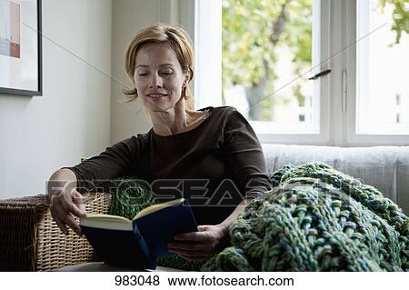 A woman reading a book while reclining on a sofa View Large Photo Image Stock Photo - A woman reading a book while reclining on a sofa. Fotosearch