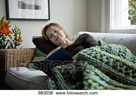A woman reading a book while reclining on a sofa View Large Photo Image Stock Photograph - A woman reading a book while reclining on a sofa. Fotosearch
