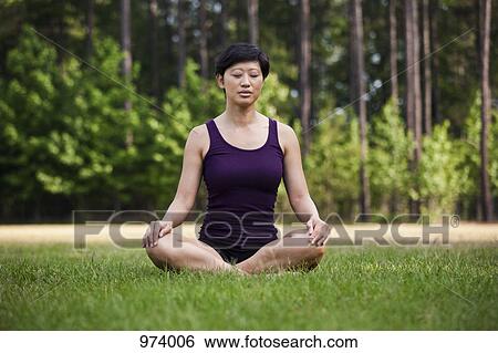 Stock Photograph - A woman sitting cross-legged on grass, eyes closed. Fotosearch