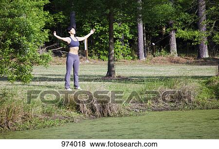 Stock Photo - A woman stretching beside a lake, eyes closed. Fotosearch