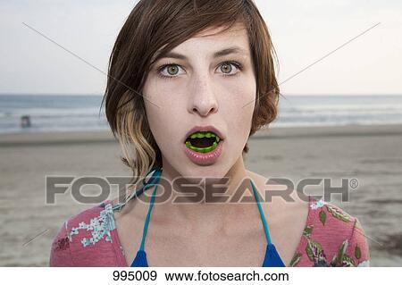 Stock Photo - A woman wearing vampire teeth at the beach, portrait. Fotosearch