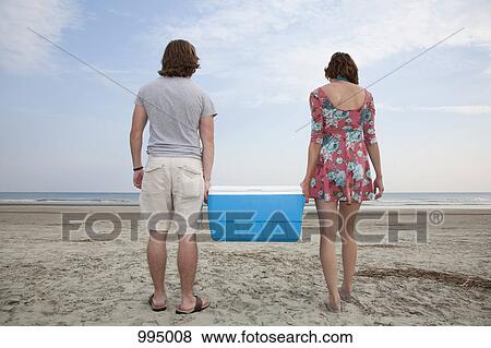 Stock Photo - A young couple carrying a cooler together on the beach. Fotosearch