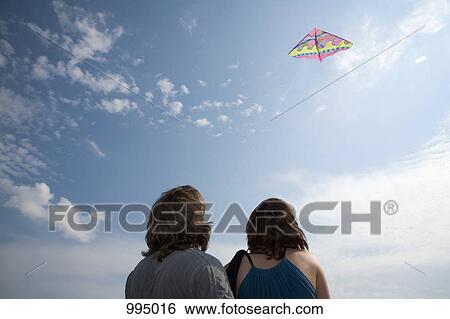A young couple flying a kite, rear view View Large Photo Image Stock Photograph - A young couple flying a kite, rear view. Fotosearch