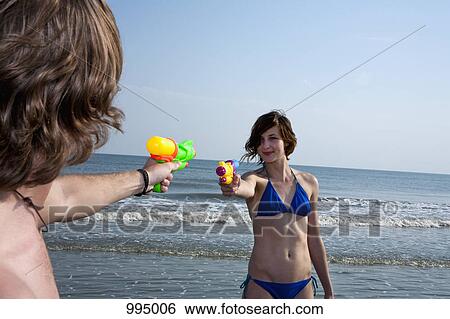 A young couple playing with squirt guns at the beach View Large Photo Image Stock Photograph - A young couple playing with squirt guns at the beach. Fotosearch