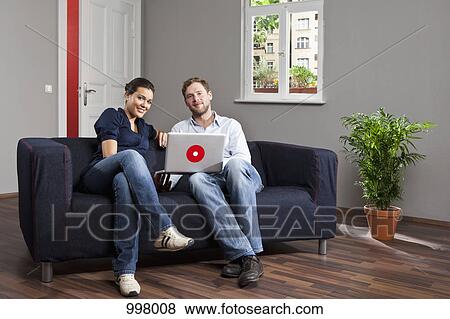 A young couple using a laptop together in their living room View Large Photo Image Stock Photo - A young couple using a laptop together in their living room. Fotosearch